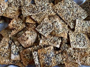 Crispy homemade seed crispbread stacked on a wooden board, showing their golden-brown color and rustic texture.