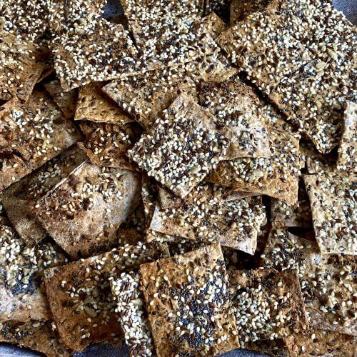 Crispy homemade seed crispbread stacked on a wooden board, showing their golden-brown color and rustic texture.