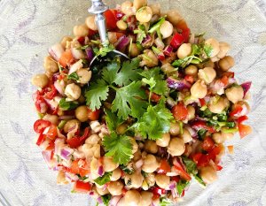 Asian-style chickpea salad with red onions, chili, cilantro, ginger, and garlic in a glass serving bowl.