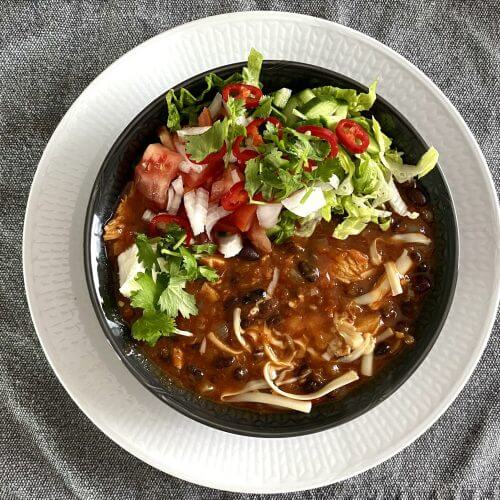 A hearty bowl of Mexican chicken chili topped with fresh cilantro, served with chopped tomatoes, cucumber, and a squeeze of lime.