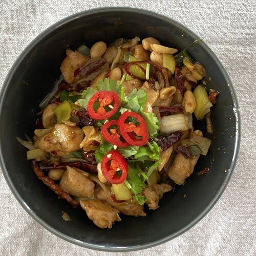 A vibrant plate of Kung Pao Chicken, topped with fresh cilantro and sliced red chilies, showcasing tender chicken pieces, roasted peanuts, and colorful bell peppers in a savory sauce.
