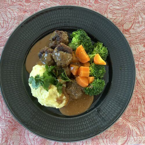 Plate of traditional Finnish meatballs served with creamy mashed potatoes, steamed carrots, and broccoli.