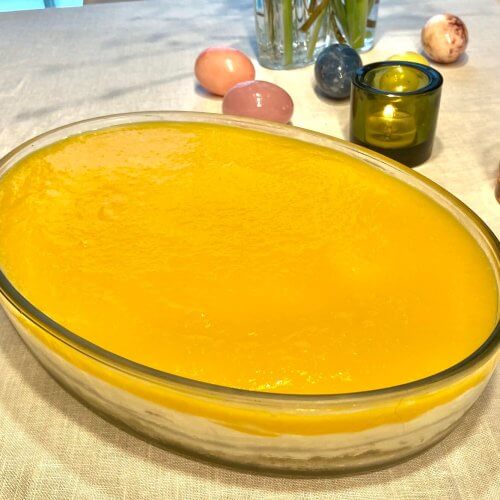 A fresh and creamy mango cheesecake topped with a smooth golden mango layer, served in a glass dish with visible layers and a walnut crunch.