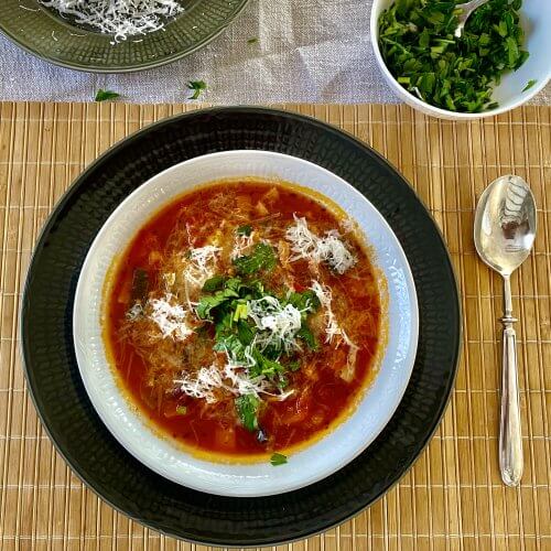 A bowl of minestrone soup topped with chopped parsley and grated Parmesan cheese.