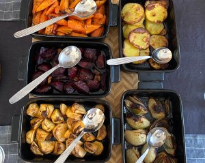 Colorful oven-roasted vegetables baked in separate oven dishes, including thinly sliced potatoes, cubed rutabaga and beets, carrot sticks, and onion wedges.