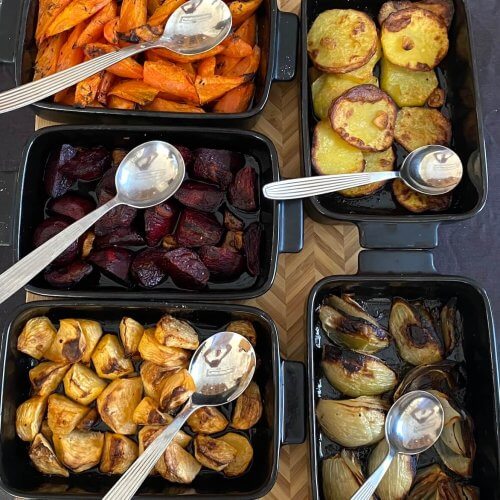 Colorful oven-roasted vegetables baked in separate oven dishes, including thinly sliced potatoes, cubed rutabaga and beets, carrot sticks, and onion wedges.