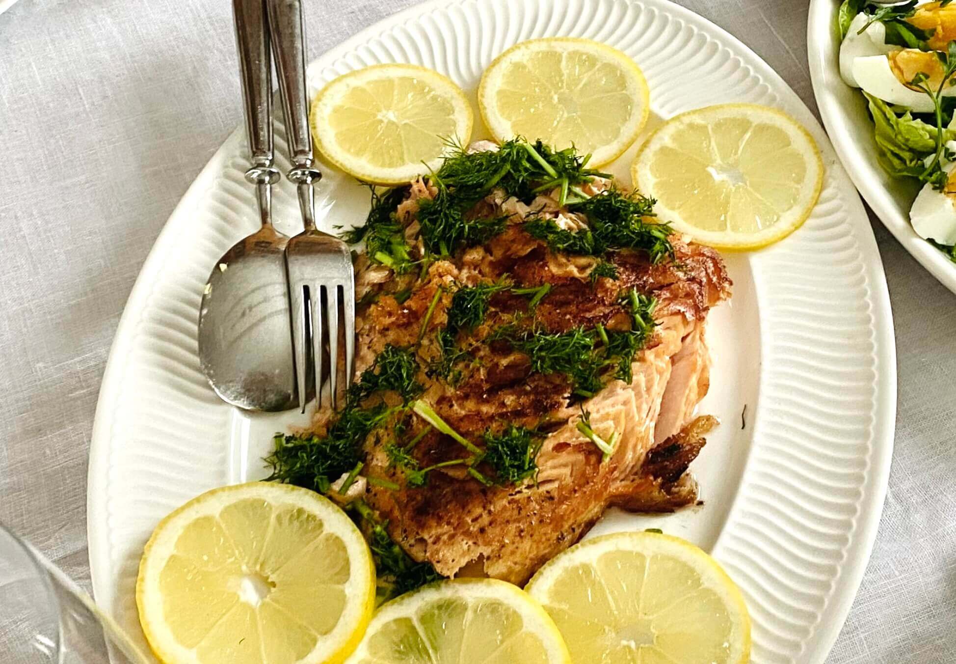 Grilled salmon fillet garnished with fresh dill and lemon slices on a serving plate.