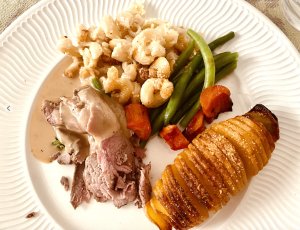 Finnish Easter plated main course with roasted lamb, hasselback potatoes, greens, gravy, and traditional macaroni casserole