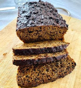 Finnish Archipelago Bread on a wooden cutting board, with several dark, moist slices cut and visible.