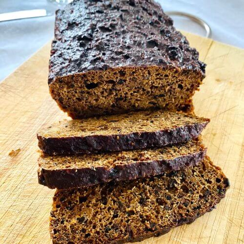 Finnish Archipelago Bread on a wooden cutting board, with several dark, moist slices cut and visible.