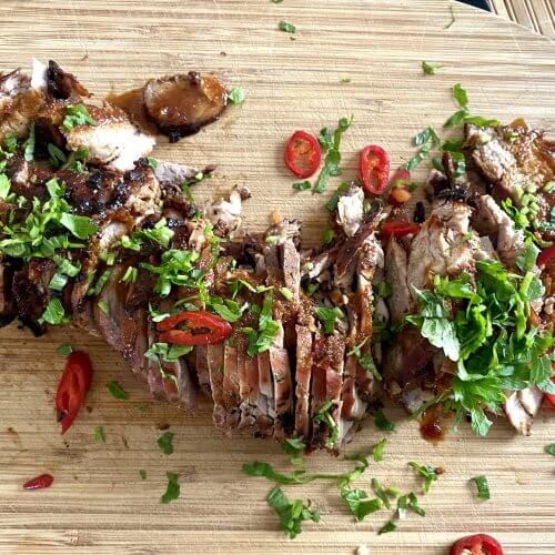 Grilled Char Siu Pork tenderloin, garnished with parsley and red chili, offering a perfect balance of smoky sweetness and a hint of spice.