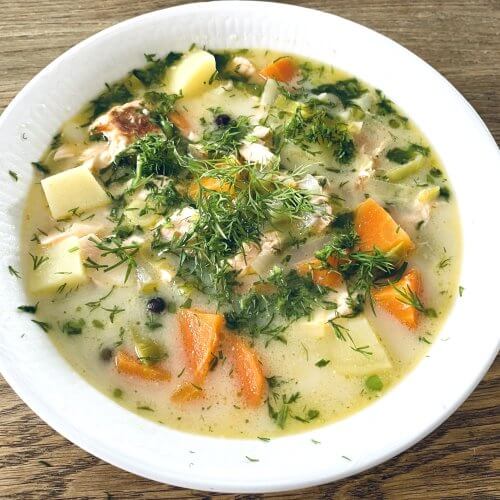 A bowl of Finnish salmon soup with chunks of salmon, potatoes, and carrots in a creamy broth, garnished with fresh dill and chives.
