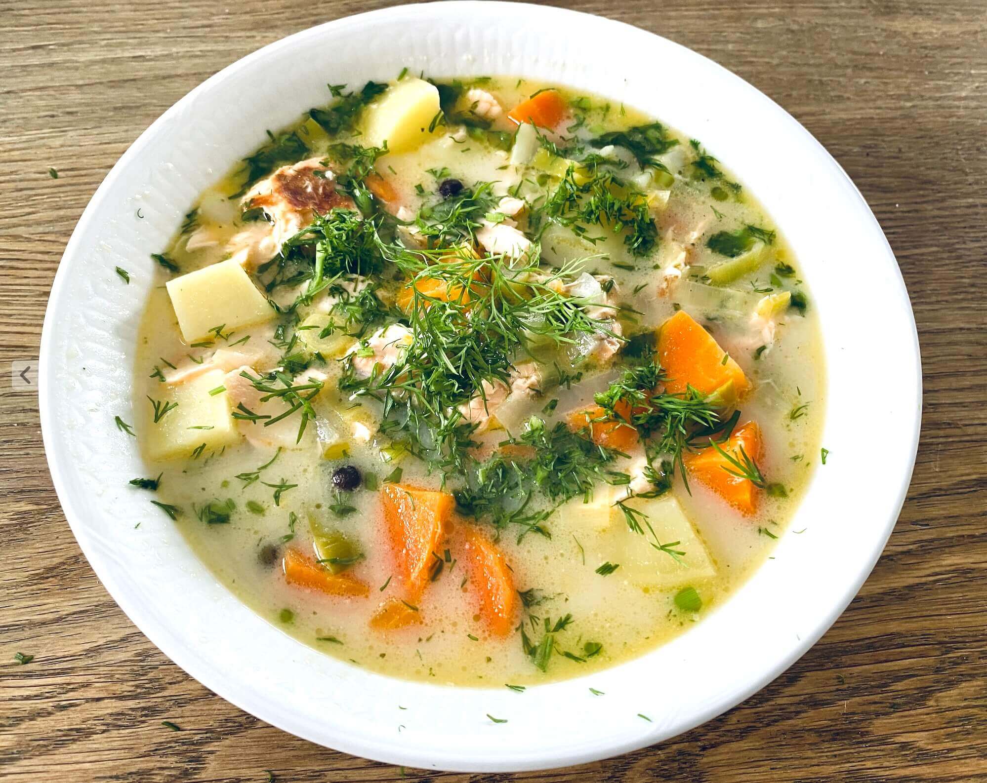 A bowl of Finnish salmon soup with chunks of salmon, potatoes, and carrots in a creamy broth, garnished with fresh dill and chives.