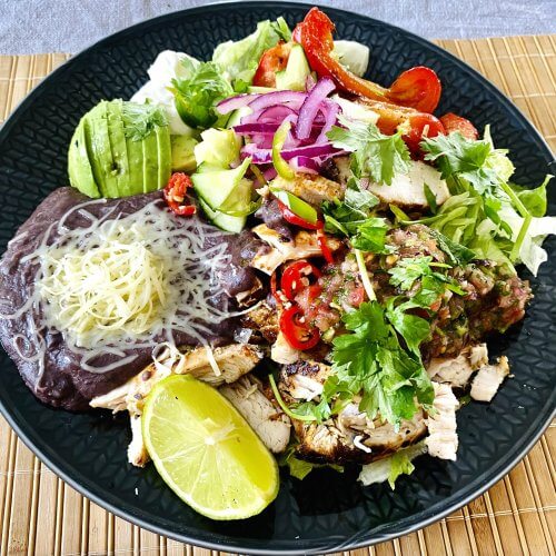 Grilled chipotle chicken salad served on a plate with black beans, avocado, cheddar, and fresh Mexican-inspired toppings.