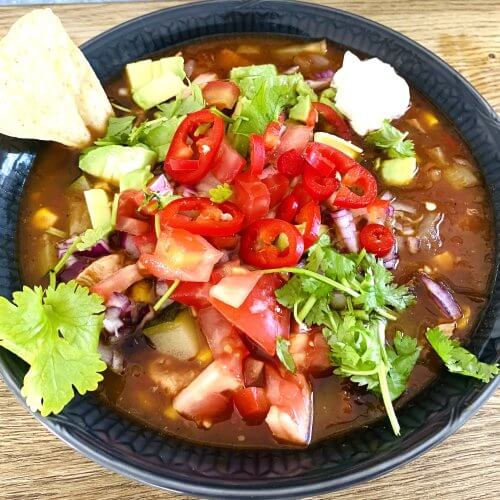 Bowl of Mexican chicken soup with corn, black beans, avocado, tomatoes, sour cream, and fresh cilantro