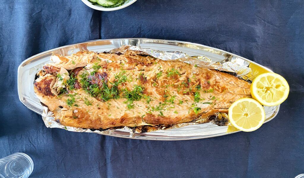 Grilled salmon fillet on a plate, garnished with lemon slices and fresh dill.