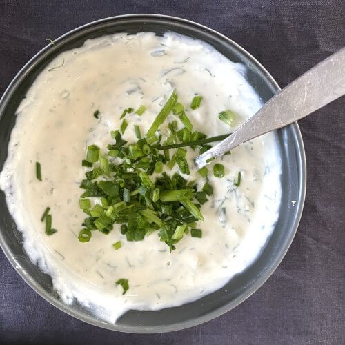 Creamy dill and horseradish sauce in a small grey bowl, garnished with fresh herbs