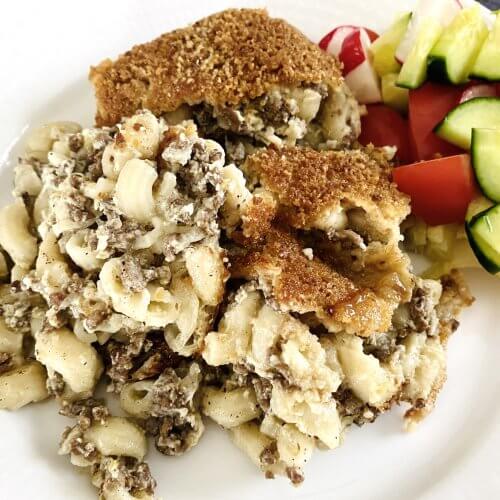 Plated Finnish meat and macaroni casserole with golden breadcrumb crust served alongside a fresh mixed green salad.