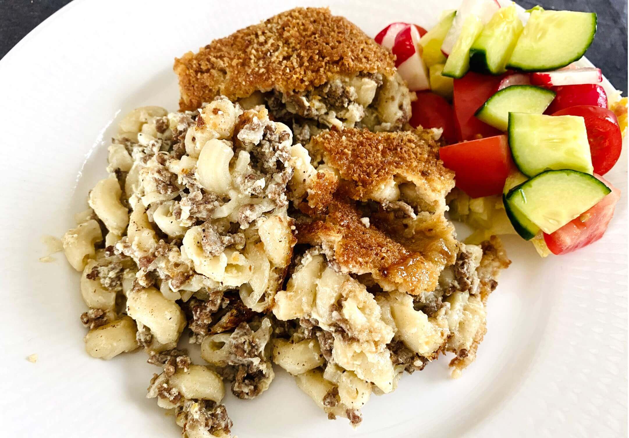 Plated Finnish meat and macaroni casserole with golden breadcrumb crust served alongside a fresh mixed green salad.