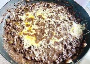 Simple refried black beans topped with melted Monterey Jack cheese in a cast-iron skillet