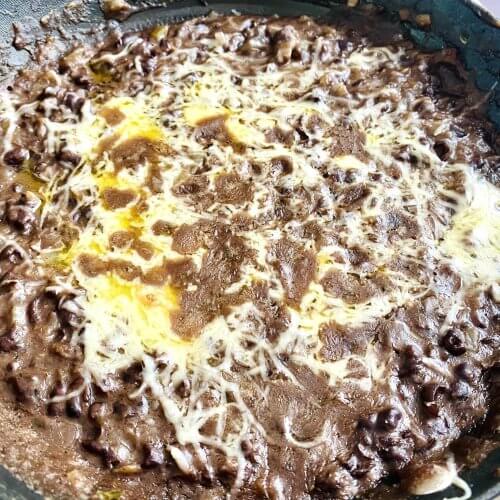 Simple refried black beans topped with melted Monterey Jack cheese in a cast-iron skillet