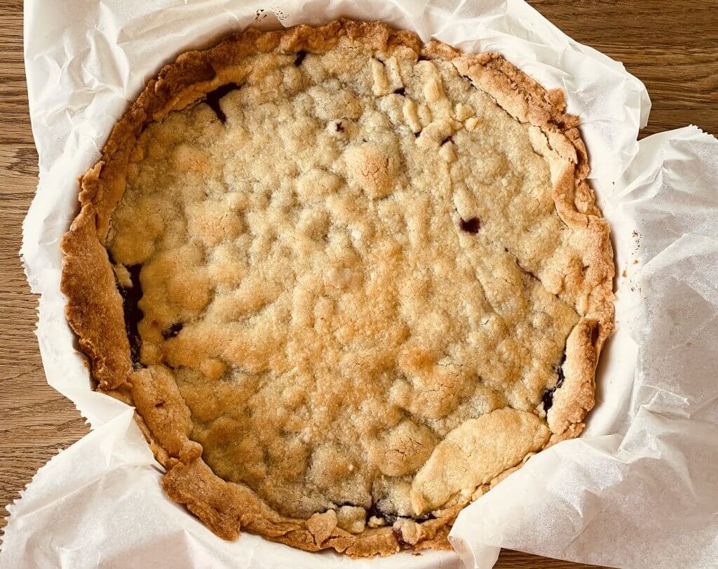 Freshly baked rustic blueberry pie in a pie tin lined with parchment paper, topped with a full golden crust.