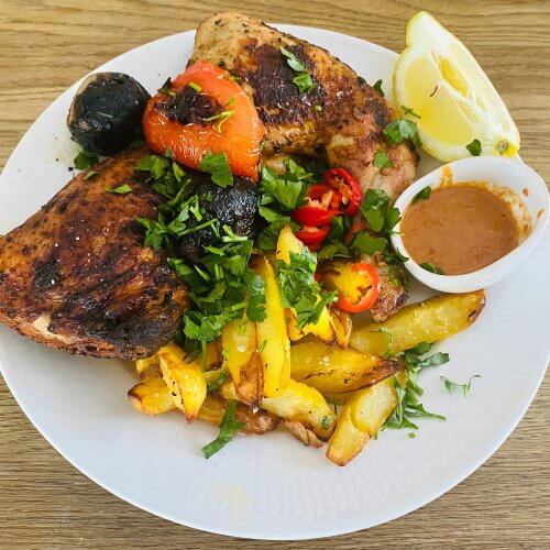 Grilled Piri Piri chicken drumsticks served with roasted potato wedges, grilled vegetables, and a small bowl of sauce on a white plate.