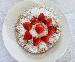 A rhubarb frangipane cake dusted with powdered sugar and garnished with whole strawberries, served on a white plate.