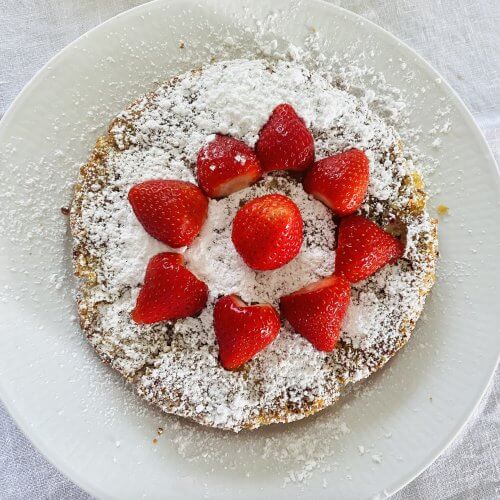 A rhubarb frangipane cake dusted with powdered sugar and garnished with whole strawberries, served on a white plate.