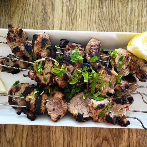 Grilled pork souvlaki skewers on a white plate, garnished with fresh lemon wedges.