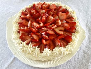 Traditional Finnish strawberry layer cake on a white serving platter, topped with fresh strawberries and whipped cream.