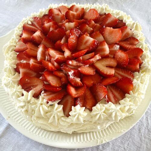 Traditional Finnish strawberry layer cake on a white serving platter, topped with fresh strawberries and whipped cream.