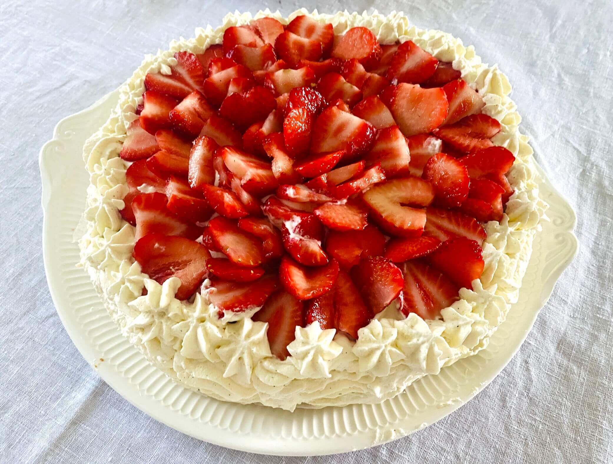 Traditional Finnish strawberry layer cake on a white serving platter, topped with fresh strawberries and whipped cream.