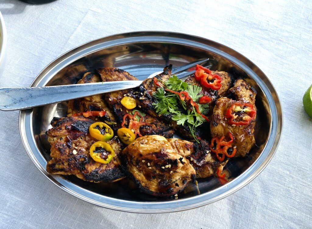 Teriyaki grilled chicken served in an oval bowl, garnished with red and yellow chilies and fresh cilantro.