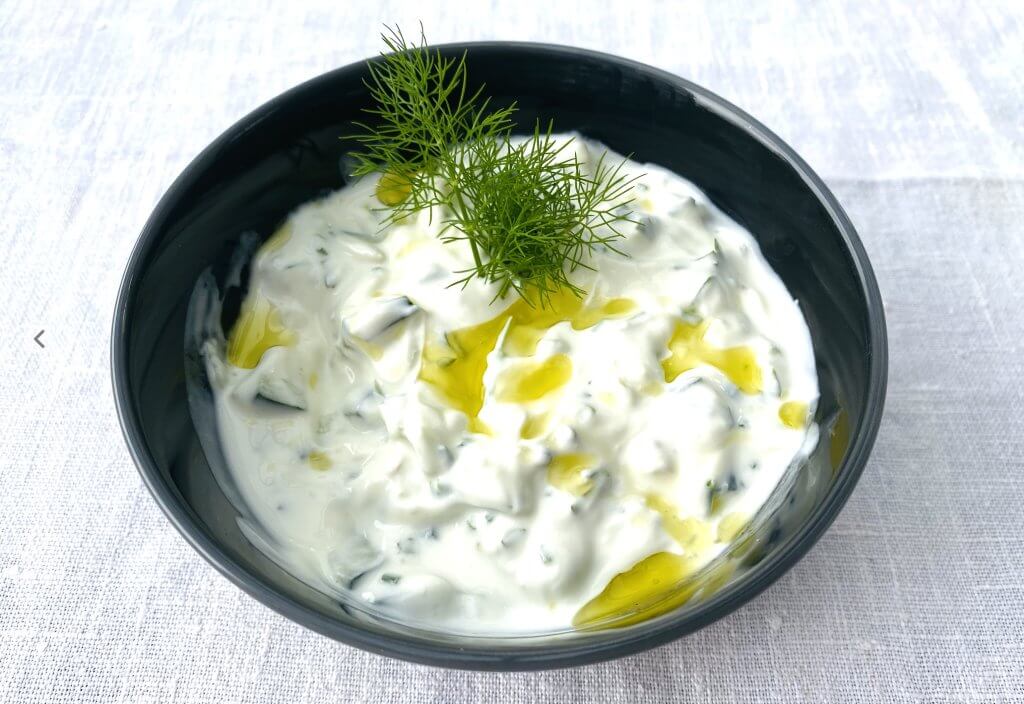 Creamy tzatziki sauce garnished with fresh dill, served in a dark grey bowl.