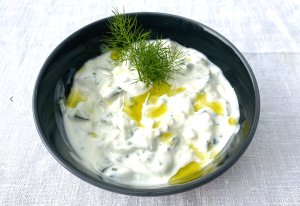 Creamy tzatziki sauce garnished with fresh dill, served in a dark grey bowl.