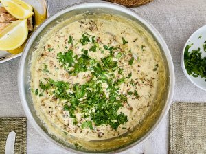 Creamy Finnish chanterelle sauce garnished with parsley, viewed from above, with grilled salmon and lemon wedges partially visible in the corner.