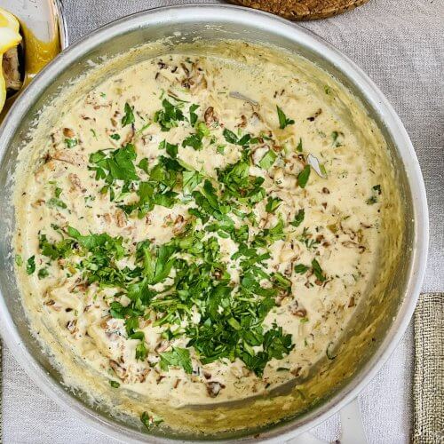 Creamy Finnish chanterelle sauce garnished with parsley, viewed from above, with grilled salmon and lemon wedges partially visible in the corner.
