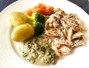 Creamy chanterelle mushroom sauce served with grilled salmon, new potatoes, boiled carrots, and broccoli on a white plate.
