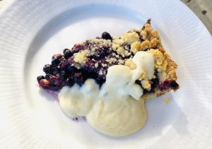 Slice of blueberry almond pie on a white plate with a generous spoonful of creamy vanilla custard sauce