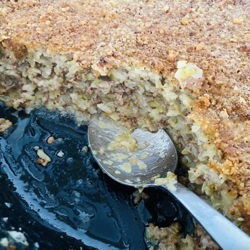 Round black ceramic oven dish with Finnish cabbage casserole, a portion removed to reveal the juicy cabbage and meat filling beneath a golden crust.