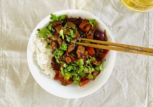 Sichuan Spicy Pork with Bell Peppers in a white bowl, served with chopsticks on the edge and a beer glass in the background.