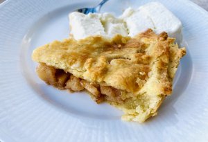 Slice of homemade apple pie with golden crust served on a white plate with a scoop of vanilla ice cream