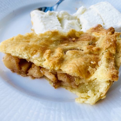 Slice of homemade apple pie with golden crust served on a white plate with a scoop of vanilla ice cream