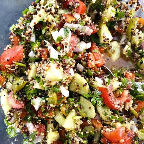 Colorful quinoa salad in a clear glass bowl with grilled zucchini, red bell pepper, cherry tomatoes, cucumber, and fresh parsley.