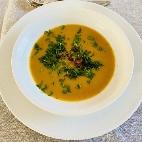 Roasted butternut squash soup in a white bowl, garnished with crispy bacon and fresh parsley.