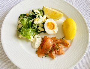 Cured Finnish salmon (gravlax) served on a white plate with boiled potato, halved boiled egg, egg salad, lemon wedge, and horseradish sauce.