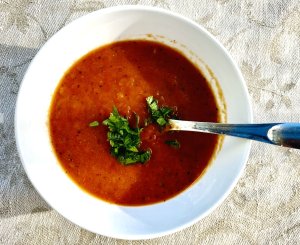 Red Espelette chili and tomato sauce in a white bowl, garnished with fresh parsley, with roasted pepper skins visible.