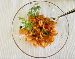 Thinly sliced Finnish gravlax (graavilohi) in a clear glass bowl, garnished with fresh dill.