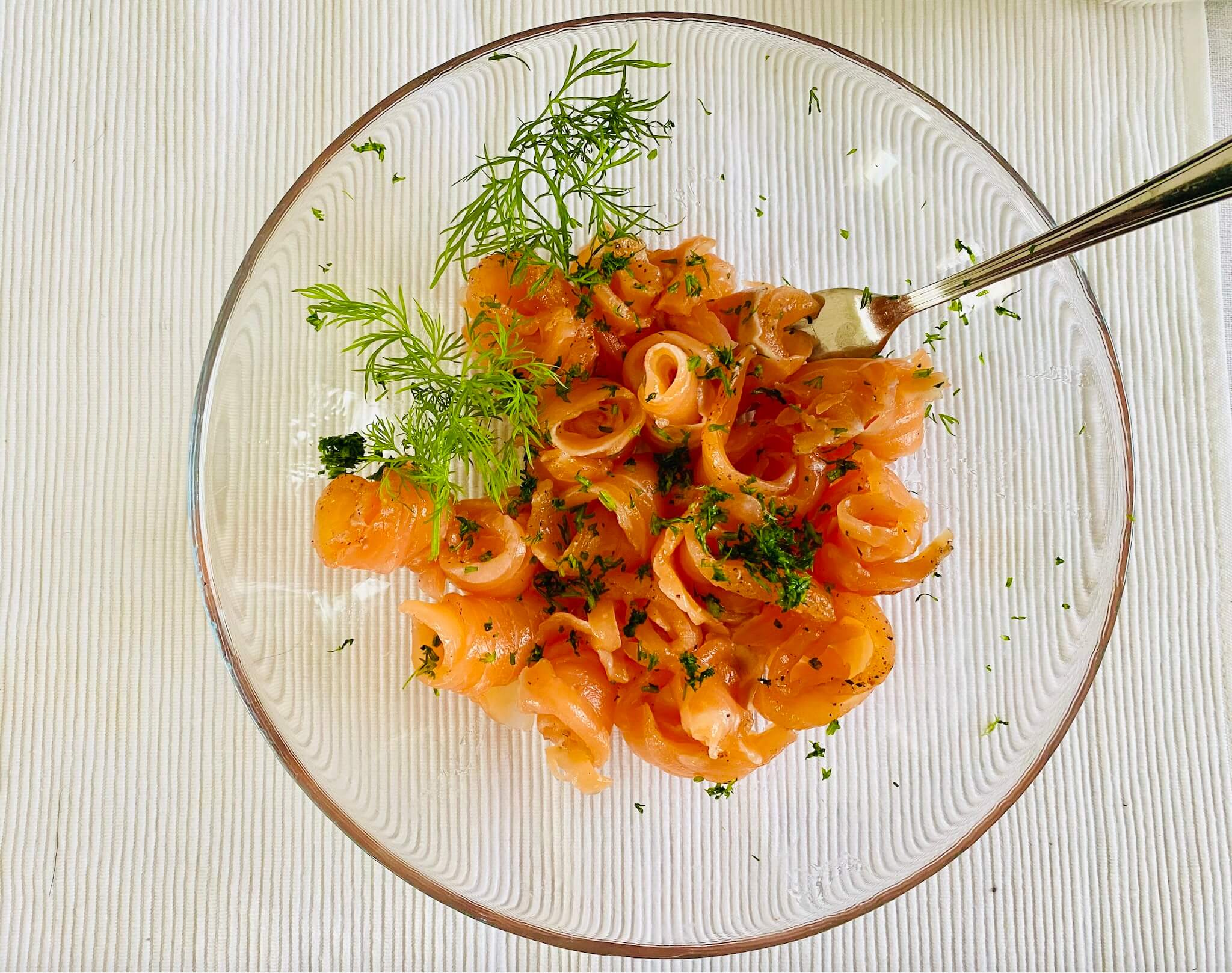 Thinly sliced Finnish gravlax (graavilohi) in a clear glass bowl, garnished with fresh dill.
